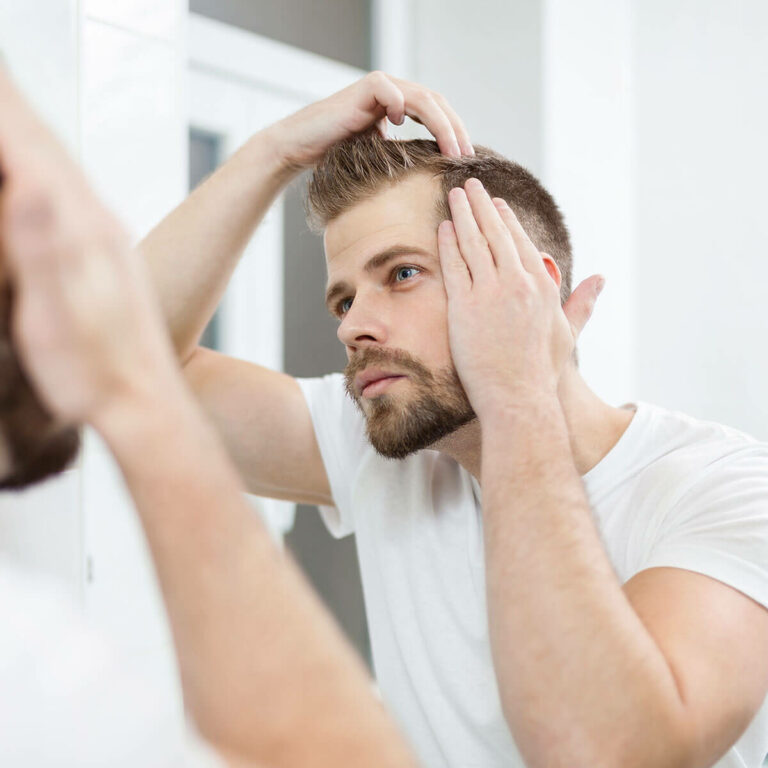 man standing in a mirror examining his hairline