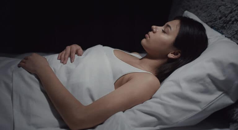 Brunette woman sleeping on her back in white cotton sheets.